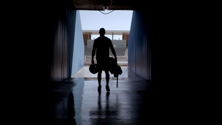 silhouette of player carrying gear entering stadium