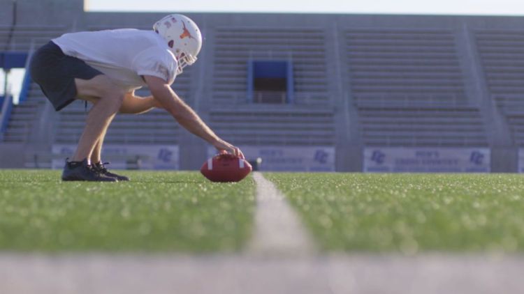 center position player bent over with hand on football in empty stadium