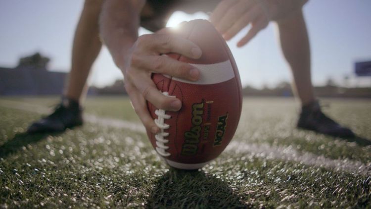 close up of football standing on end being held up by player