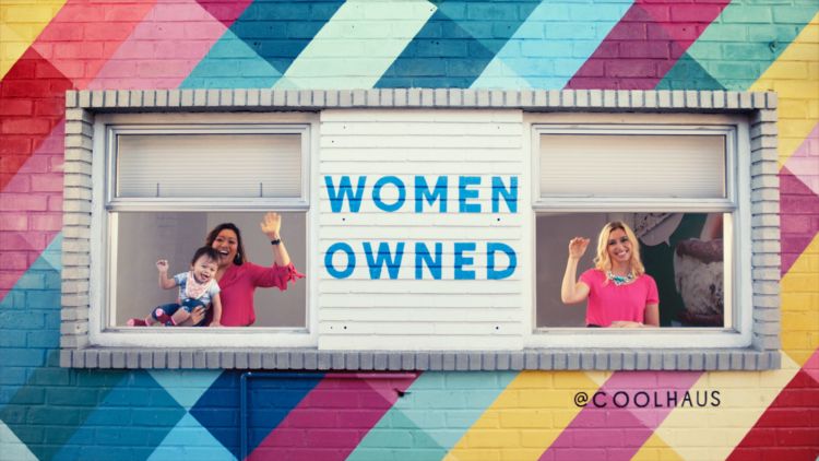 2 women and a child waving through windows. Colorful wall reads "Women Owned" @coolhaus