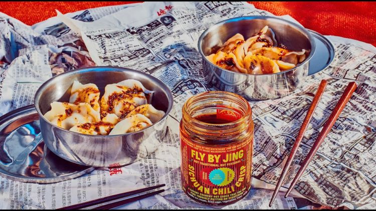 Photo of dumplings with Fly By Jing sauce, and a jar of Fly By Jing Sichuan Chili Crisp sauce.
